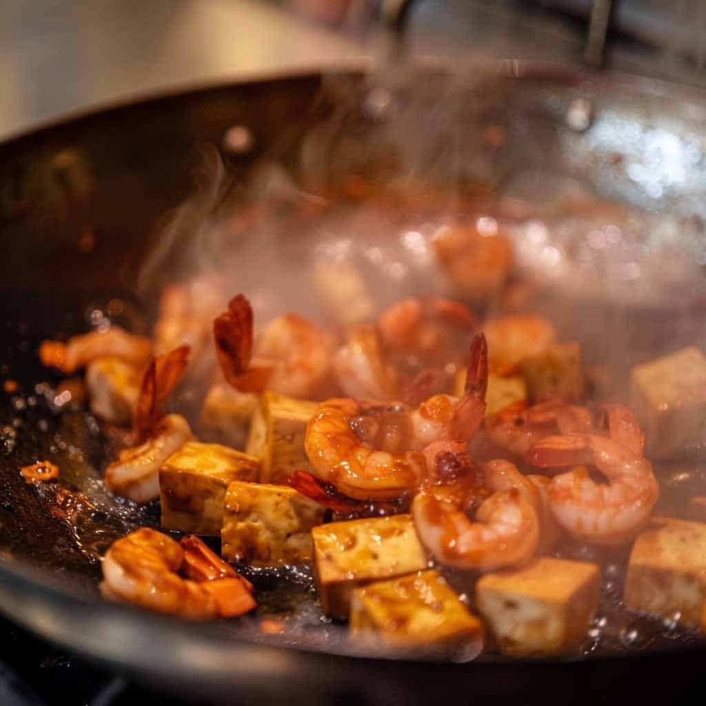Shrimp and tofu sizzling in a wok, preparing to be combined with other ingredients.