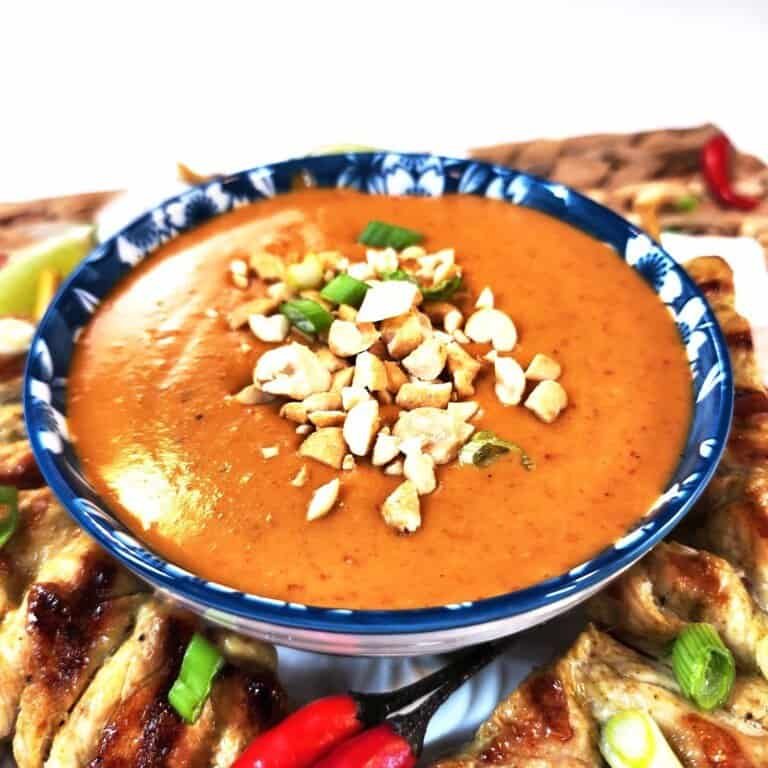 Creamy Thai peanut sauce in a rustic ceramic bowl, topped with crunchy crushed peanuts and fresh cilantro leaves, displaying rich amber color and smooth texture