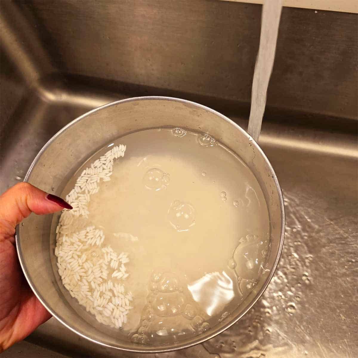 rinsing sweet rice in a bowl under running water, removing excess starch to prepare for cooking."
