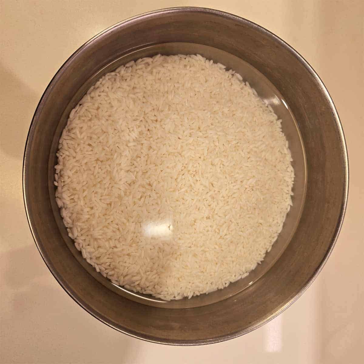 Sweet rice soaking in a bowl of water for 24 hours, with grains fully submerged and starting to absorb the water.