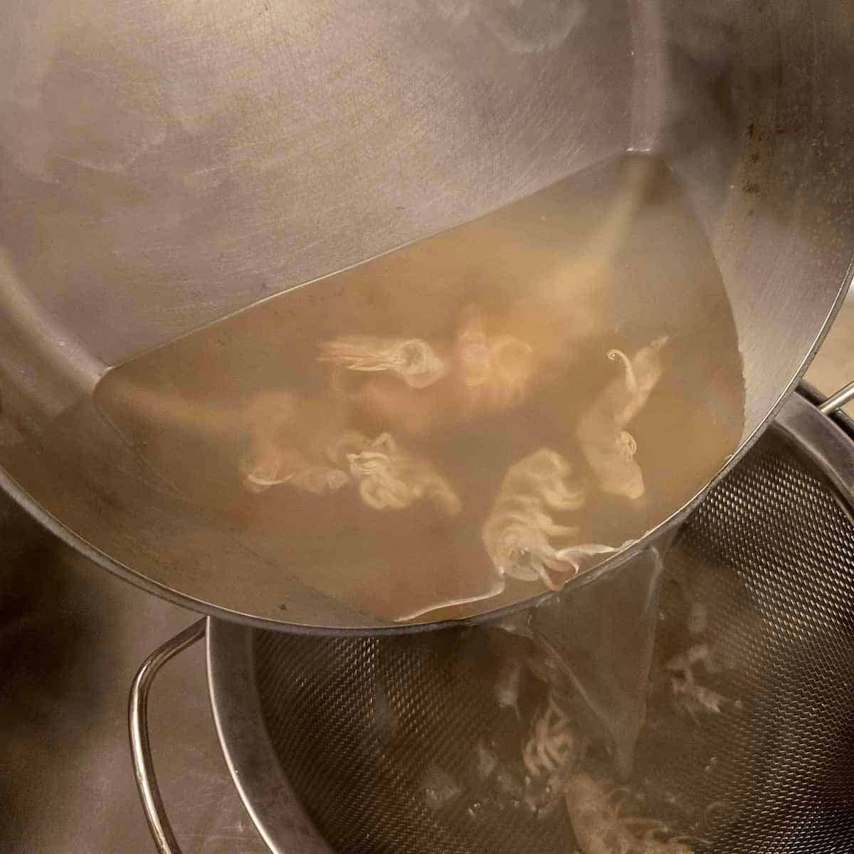 Straining shrimp shells from clear broth over a kitchen sink, using a metal sieve