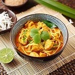 A plate of Thai Curry Noodles: stir-fried noodles with tofu, curry sauce, fresh veggies, garnished with cilantro and lime wedges