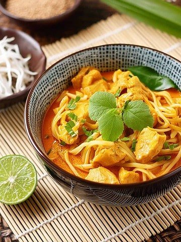 A plate of Thai Curry Noodles: stir-fried noodles with tofu, curry sauce, fresh veggies, garnished with cilantro and lime wedges