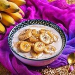 Bowl of bananas and coconut milk on a purple tablecloth.