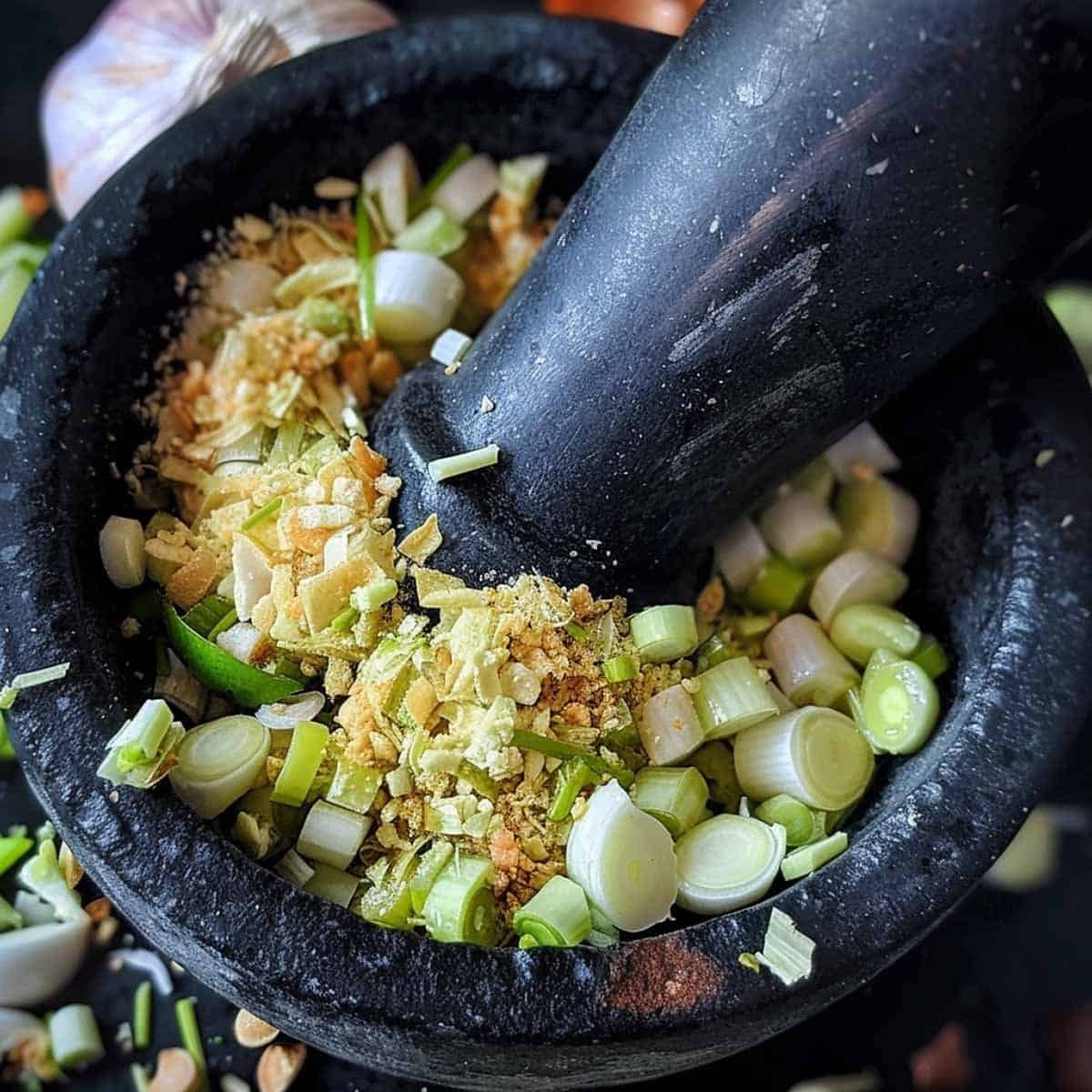 Garlic, shallots, lemongrass, galangal, and kaffir lime zest being ground with mortar and pestle to make chili paste