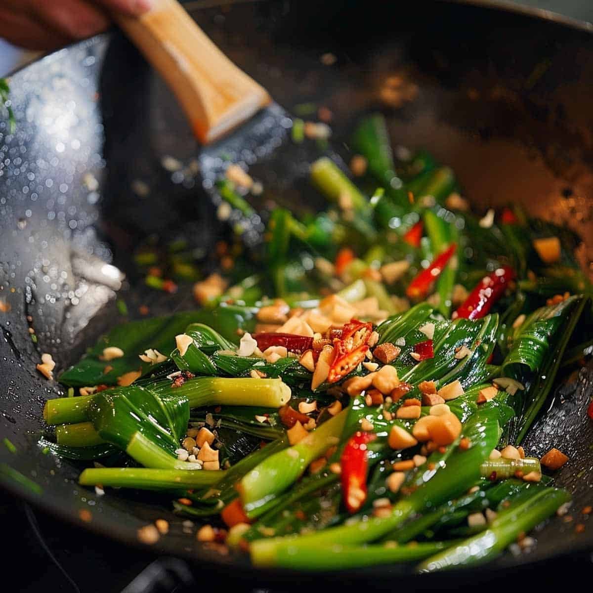Tossing fresh morning glory in a wok to coat the leaves and stems with garlic and chili-infused oil