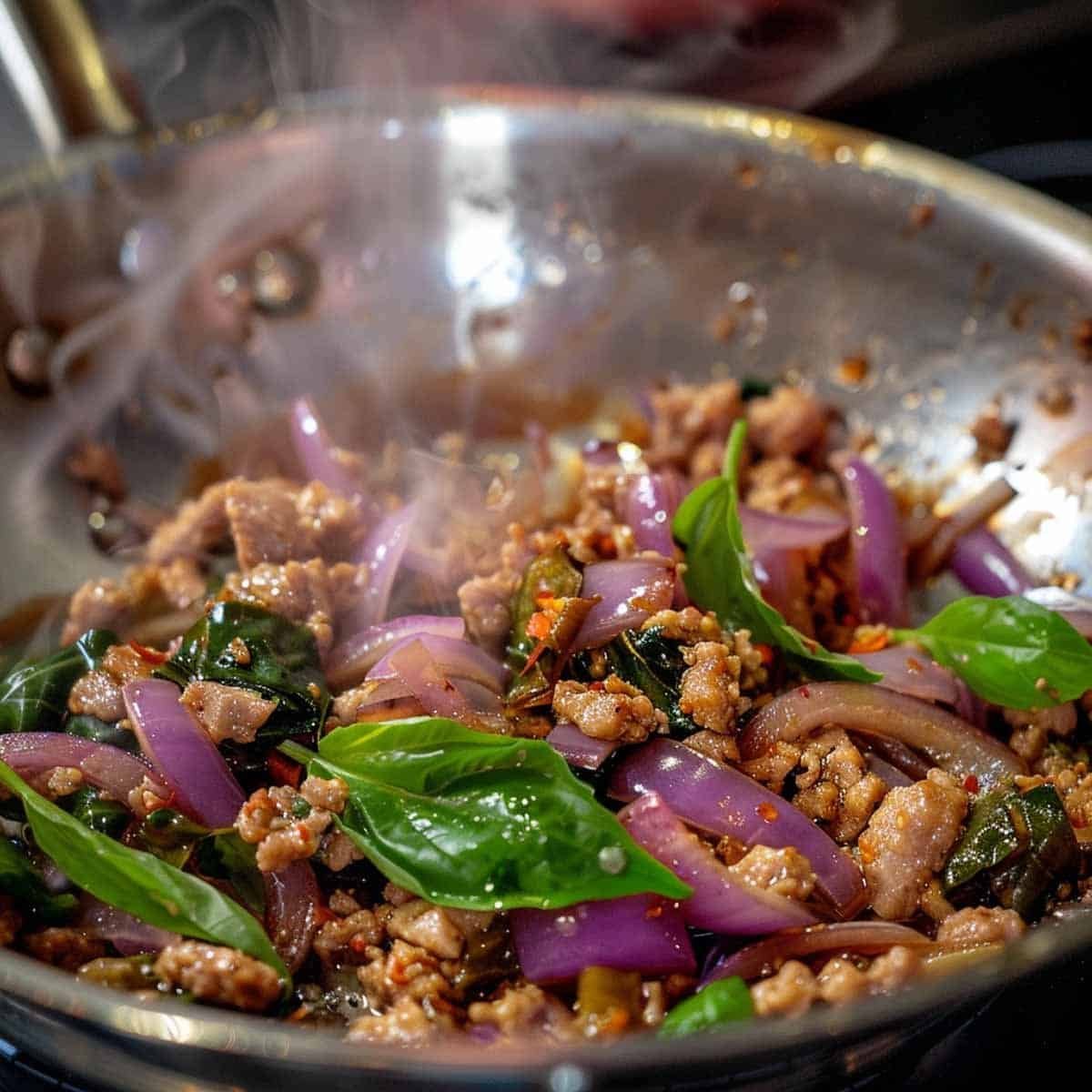Adding basil leaves to cooked pork and onions for Thai Basil Pork recipe  (Pad Kra Pao Moo)