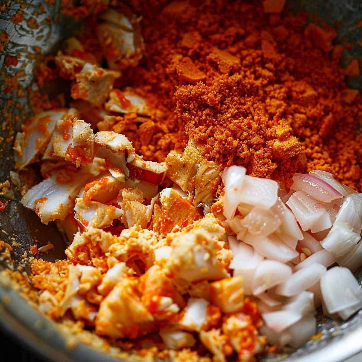 Finely chopped white fish fillets in a large mixing bowl with red curry paste, egg, fish sauce, and sugar