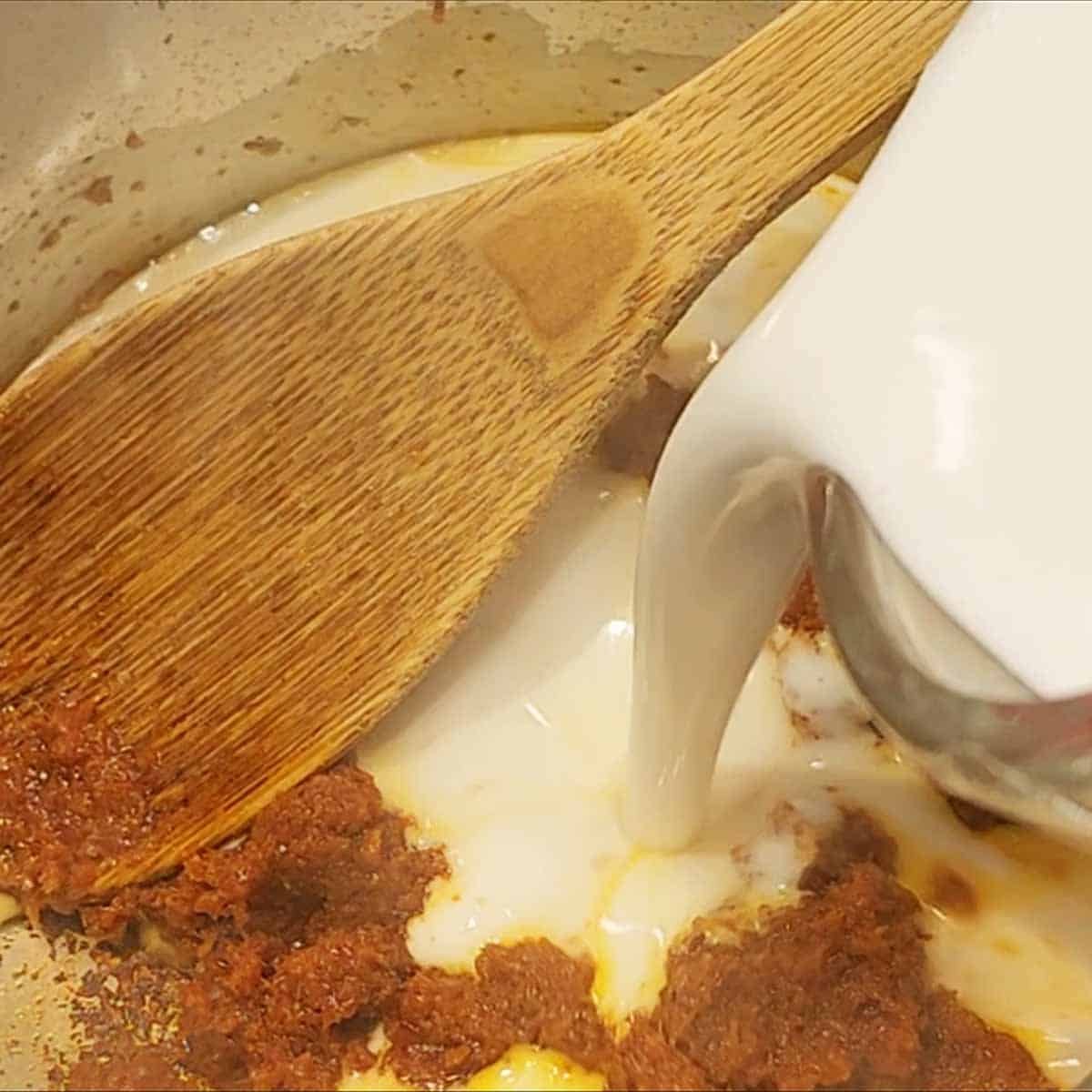 Adding coconut milk to curry to make peanut sauce 