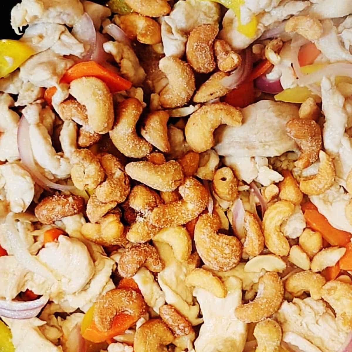 Here's the updated alt text with cashews included:
"Stir-frying chicken strips, yellow and red bell peppers, and golden cashews sizzling in a steaming wok