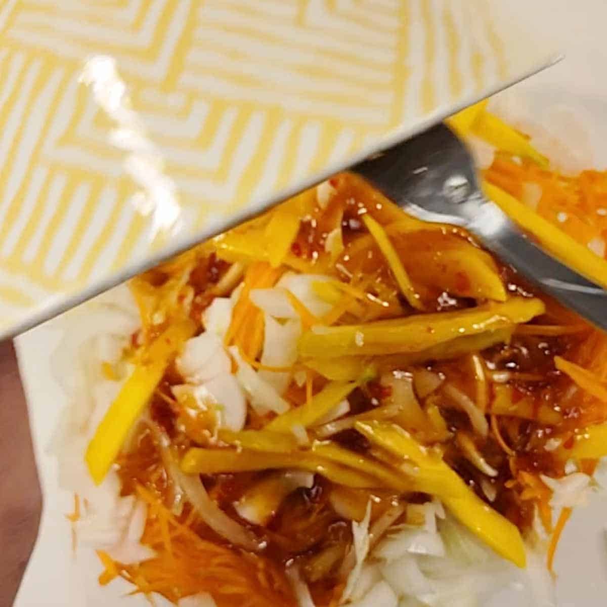 Dressing being drizzled over fresh cabbage and carrot slaw