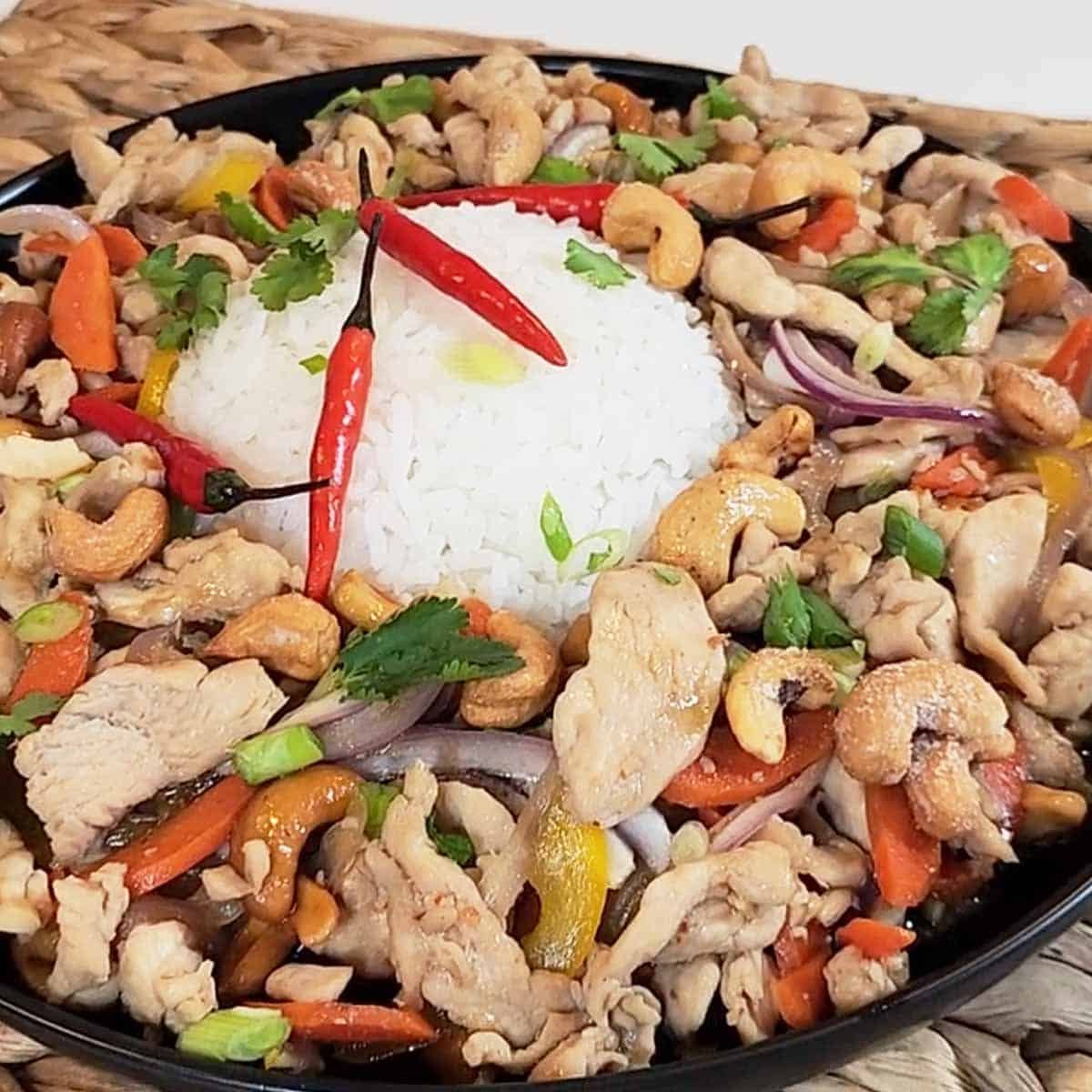 Thai Cashew Chicken with tender meat, colorful peppers, and toasted cashews served over white jasmine rice on a black ceramic plate