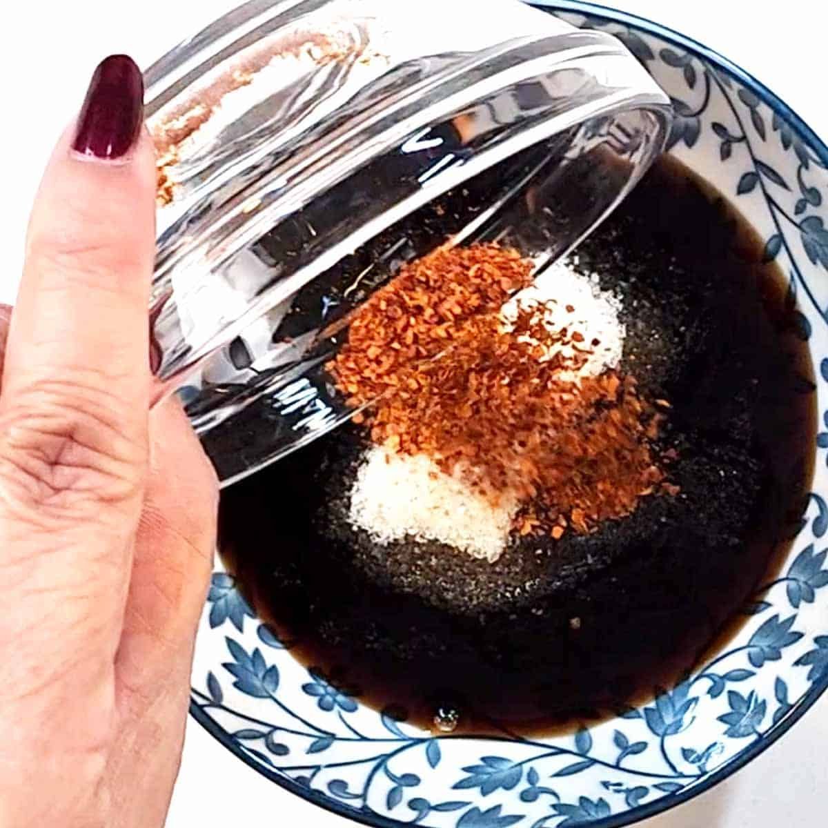 Thai sauce ingredients in small glass prep bowl: oyster sauce, soy sauce, fish sauce, sugar, and chili flakes being stirred together to a glossy dark brown blend