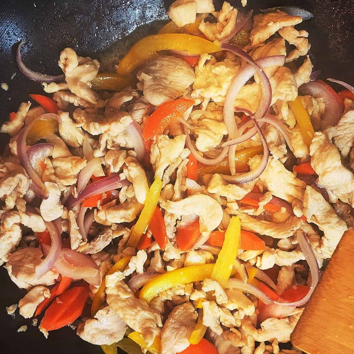 tir-frying chicken strips with yellow and red bell peppers sizzling in a steaming wok