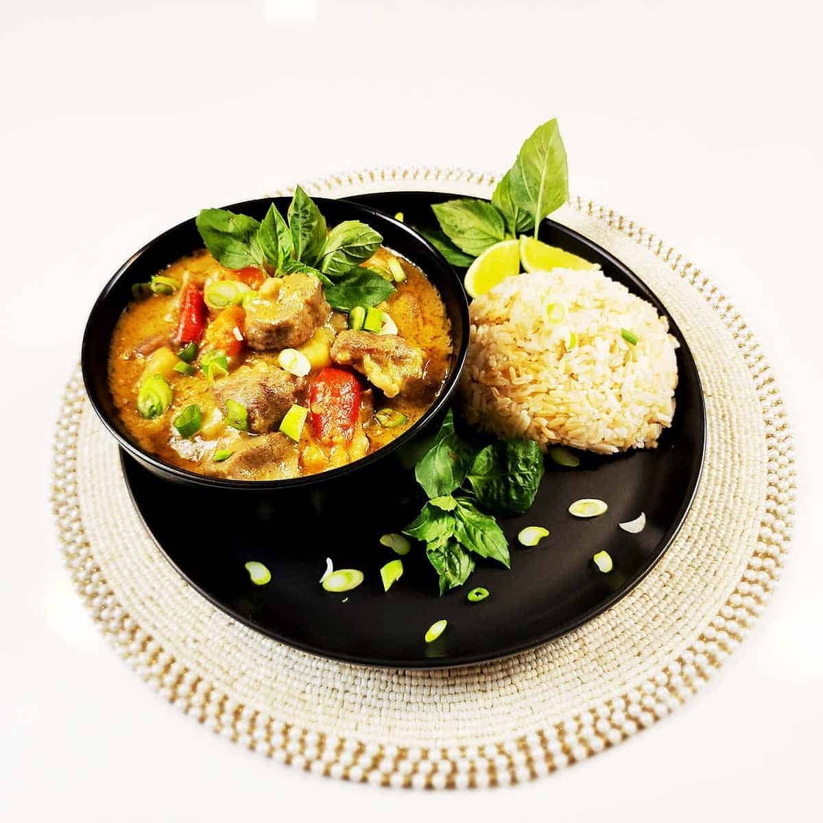 Thai yellow curry with tender pork served in black bowl beside white rice - rich golden sauce glistening with aromatic spices