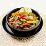 Purple eggplant stir fry with bell peppers, green onions and sesame seeds in a black bowl