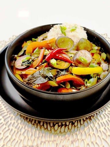 Purple eggplant stir fry with bell peppers, green onions and sesame seeds in a black bowl