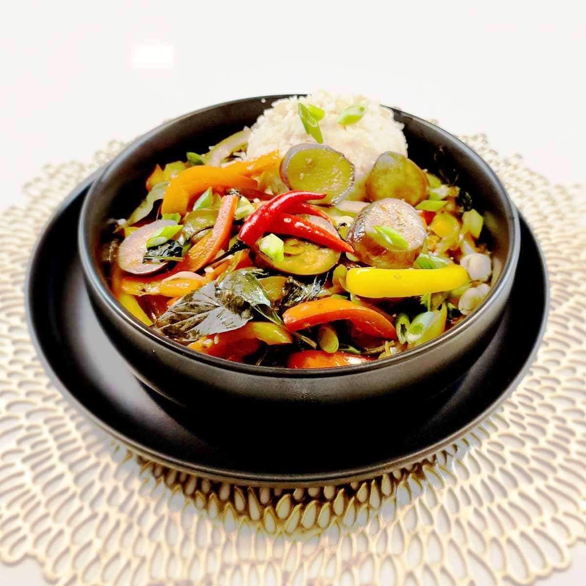 Purple eggplant stir fry with bell peppers, green onions and sesame seeds in a black bowl