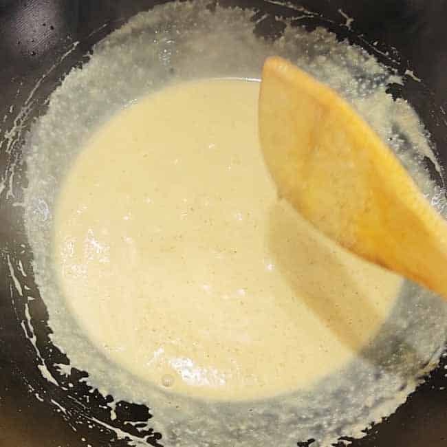 Yellow coconut curry base cooking in large pot - golden mixture of curry paste and coconut milk simmering at edges with wooden spoon