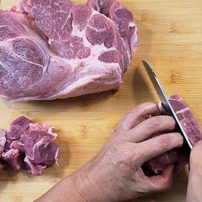 Chef's knife slicing ingredients on bamboo cutting board - fresh food preparation with wooden grain texture visible.