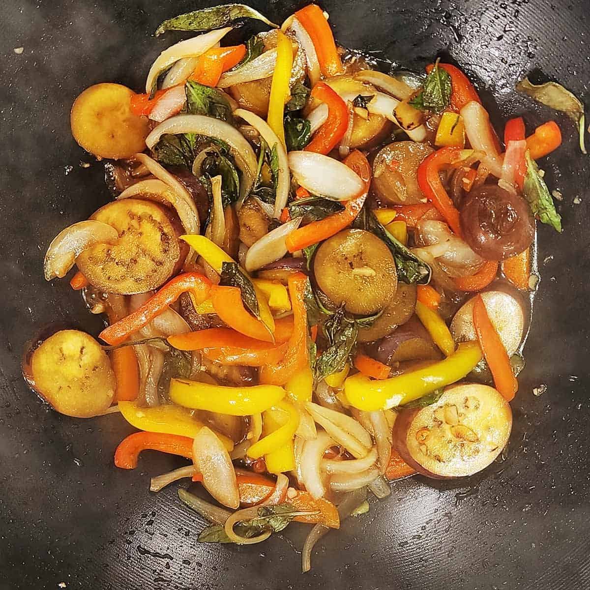 Completed Thai eggplant stir fry with glossy sauce coating vegetables in steaming wok