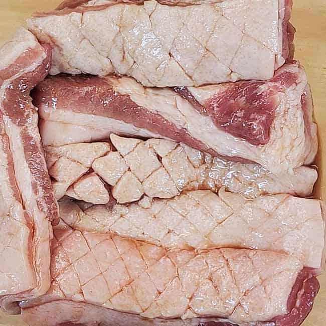 Applying flavorful marinade to the meat side of Thai pork belly while keeping the scored skin dry for perfect Moo Krob crackling