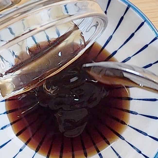 Whisking Thai pork belly marinade ingredients to combine fish sauce, oyster sauce and sugar for authentic Moo Krob recipe