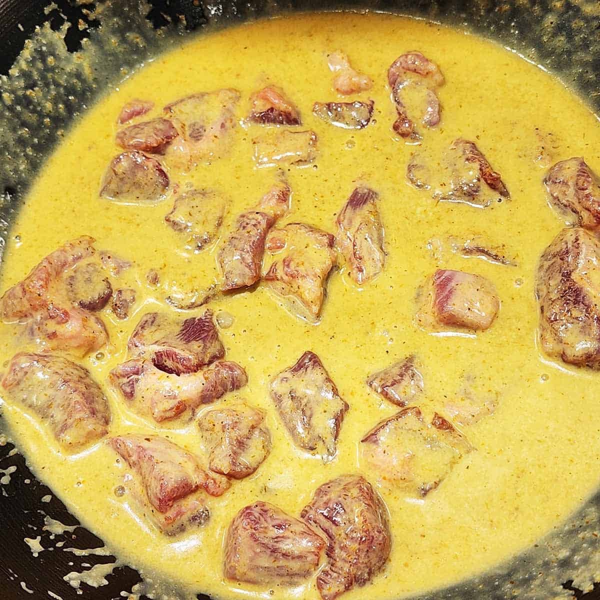 Here's a revised alt text under 125 characters:
"Pork pieces being folded into golden curry sauce - meat gently incorporated into fragrant coconut broth creating a harmonious dish.