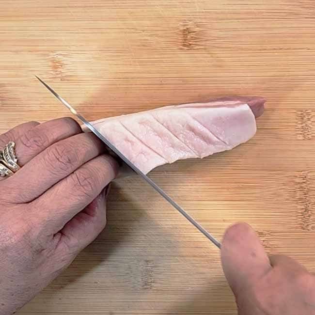 Scoring the pork belly skin in crosshatch pattern to create perfect crackling for authentic Moo Krob recipe"