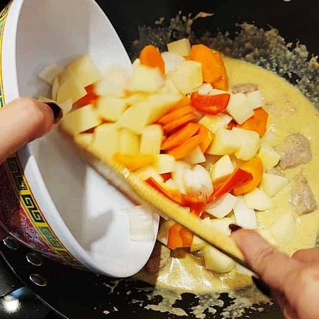 Colorful vegetables being added to hot wok - fresh ingredients tumbling into sizzling pan during Asian cooking preparation