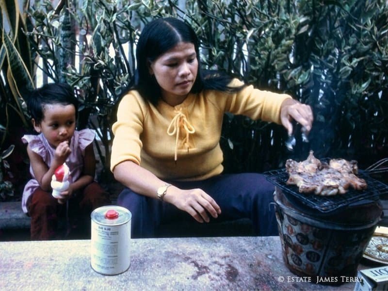 Pien cooking over charcoal grill with young Susie, Korat Thailand 1971