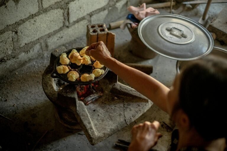 A person cooks traditional Vietnamese food on a rustic charcoal stove indoors.
