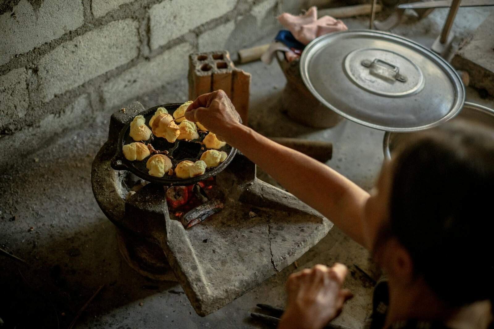 A person cooks traditional Vietnamese food on a rustic charcoal stove indoors.